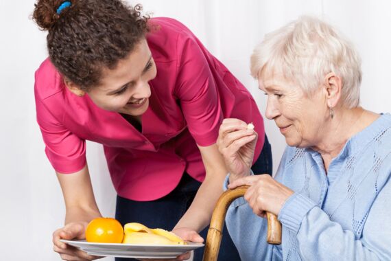 Frau reicht Seniorin Teller mit Obst