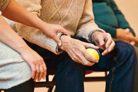 Betreuungskraft berührt eines Pflegebedürftigen, der einen Stressball in der Hand hält