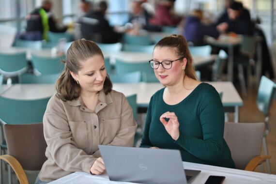 Zwei Frauen sitzen am Computer und reden über ein Thema.