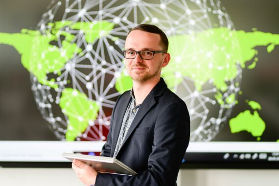 junger Mann mit Brille vor einer vernetzten Weltkarte