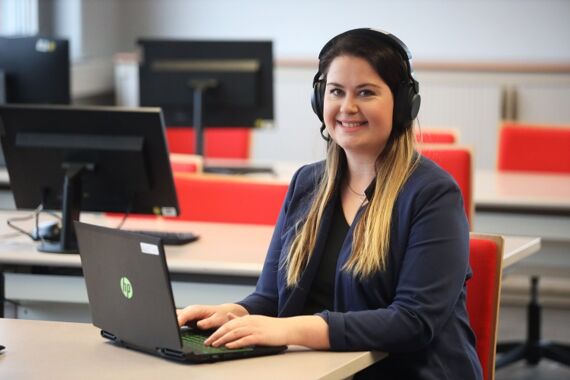 Frau mit Headset sitzt vor einem Laptop