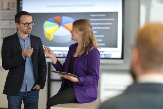 Mann und Frau stehen vor einem Smartboard